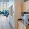 A black soft pod brewer sits on a break room counter in a car dealership as a man walks by in the background.